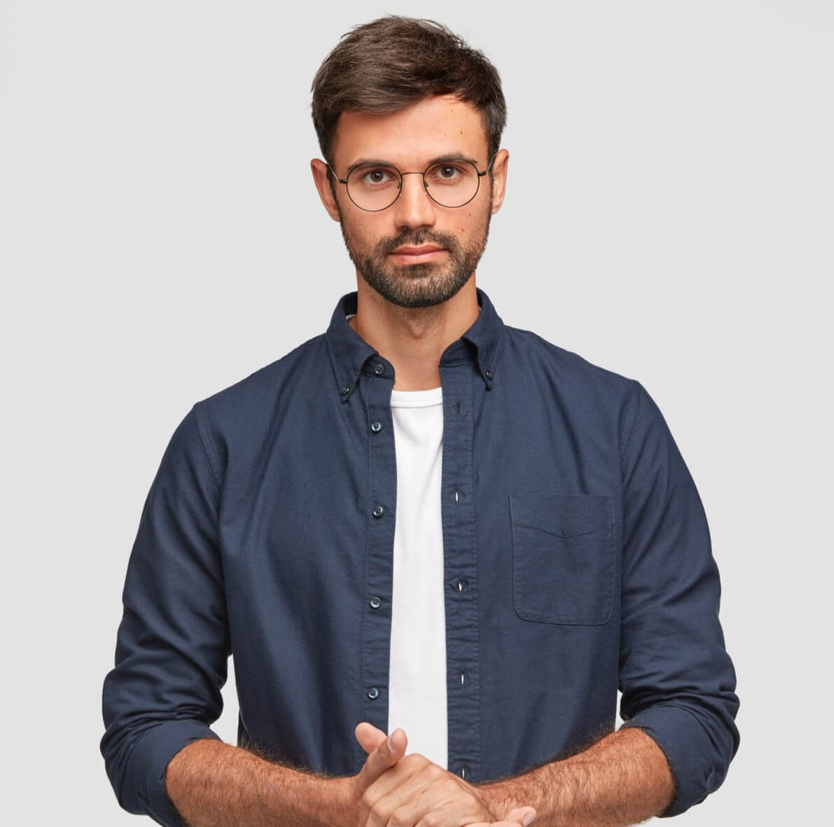 waistupportraithandsomeseriousunshavenmalekeepshandstogetherdresseddarkblueshirthastalkwithinterlocutorstandsagainstwhitewallselfconfidentmanfreelancer_m0mzq_1191